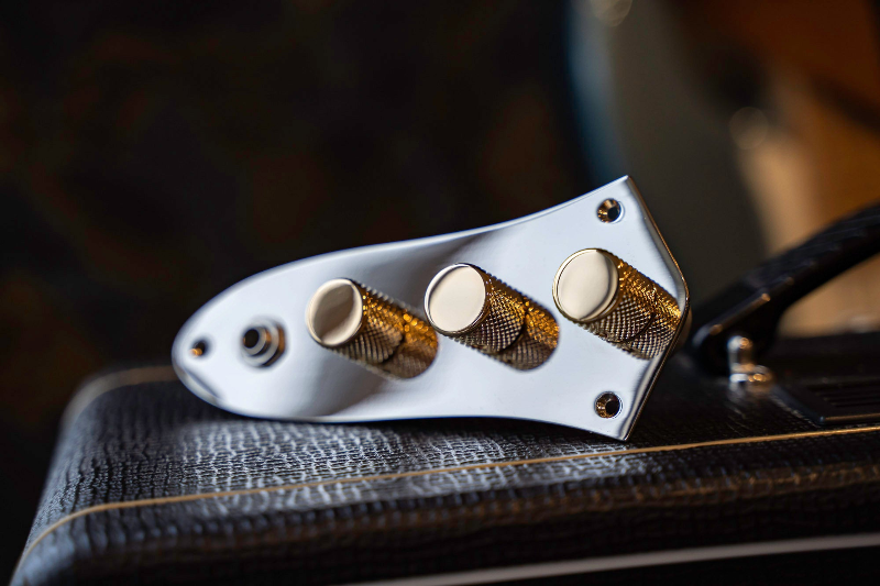 loaded control plate for Jazz bass with chrome plate and gold knurled knobs, resting on a black amp.