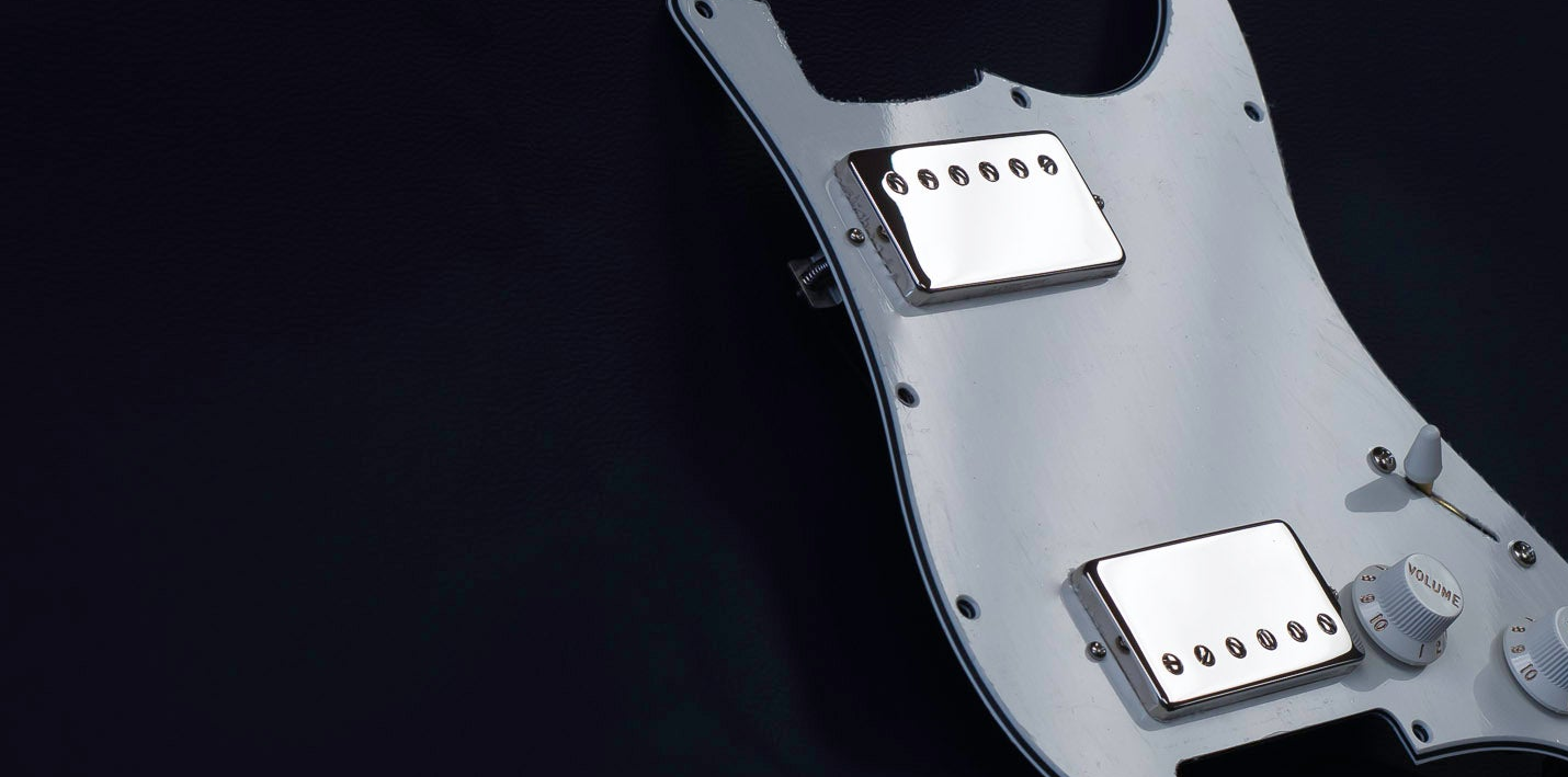 Obsidianwire custom loaded pickguard in parchment with two nickel covered humbuckers, on a dark blue background