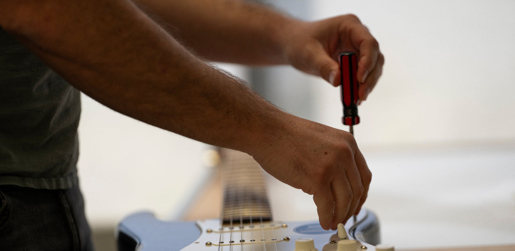 A man removing the pickguard from a black fender stratocaster.